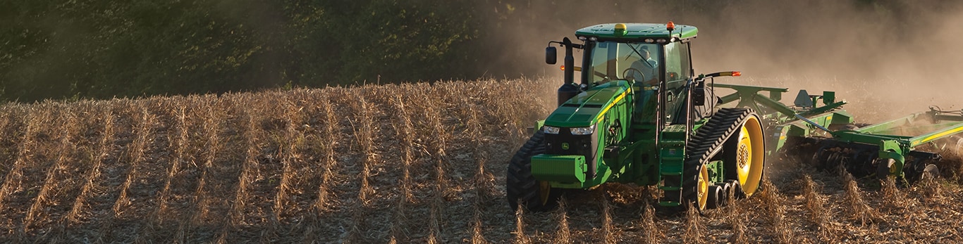 Ένα τρακτέρ John Deere κινείται μέσα σε έναν ήδη θερισμένο αγρό