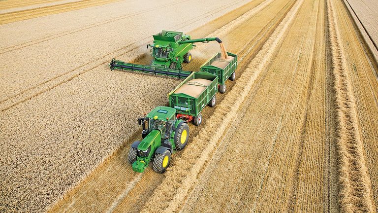 Θεριζοαλωνιστική John Deere σειράς S που εκφορτώνει σιτάρι σε δύο ρυμούλκες που ρυμουλκούνται από τρακτέρ