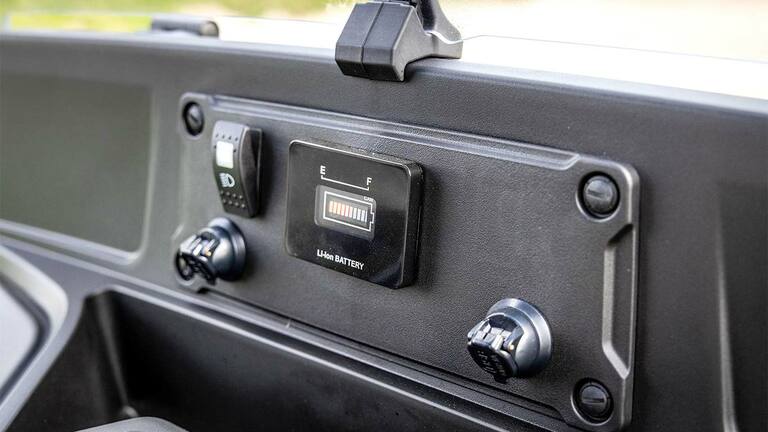 Ταμπλό ενός ηλεκτρικού μοντέλου Gator GS της John Deere που δείχνει την ένδειξη στάθμης μπαταρίας και τις θύρες τροφοδοσίας.