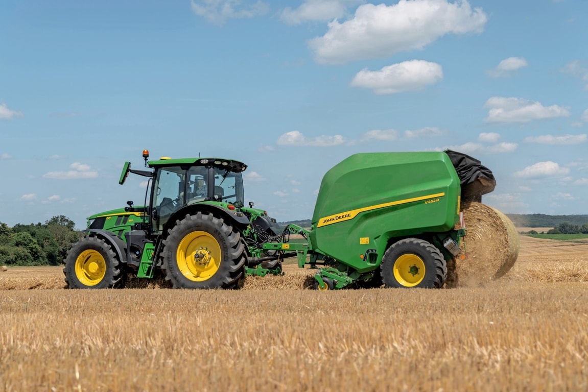 John Deere V452R σε έναν αγρό άχυρου που ρυμουλκείται από ένα John Deere 6R 150 που εξάγει ένα δέμα