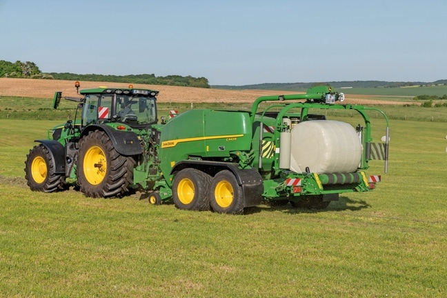 Τυλικτικό μπάλας John Deere C442R που ρυμουλκείται από ένα 6R 185 της John Deere που κάνει δέματα ενσιρώματος υψηλής πυκνότητας