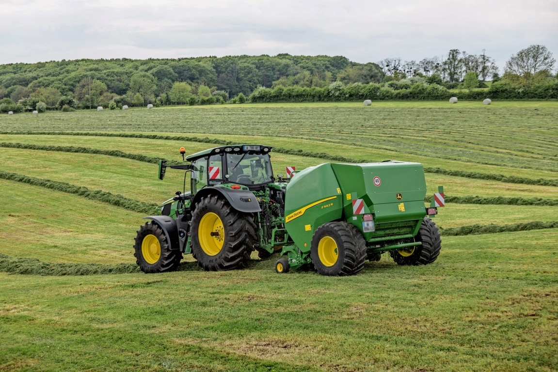 Χορτοδετικό John Deere F442R που ρυμουλκείται από ένα τρακτέρ 6M της John Deere σε λοφώδες χωράφι