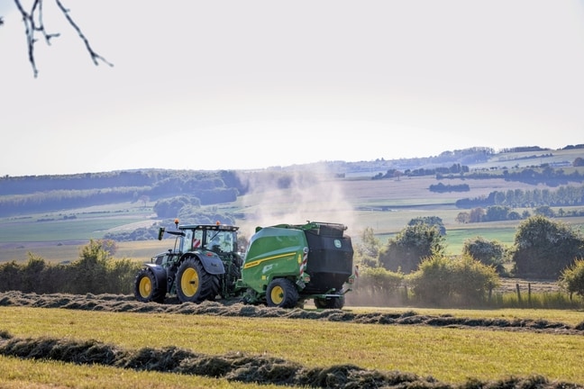 John Deere V462R που ρυμουλκείται από ένα τρακτέρ 6R 185 της John Deere για σχηματισμό δεμάτων σανού